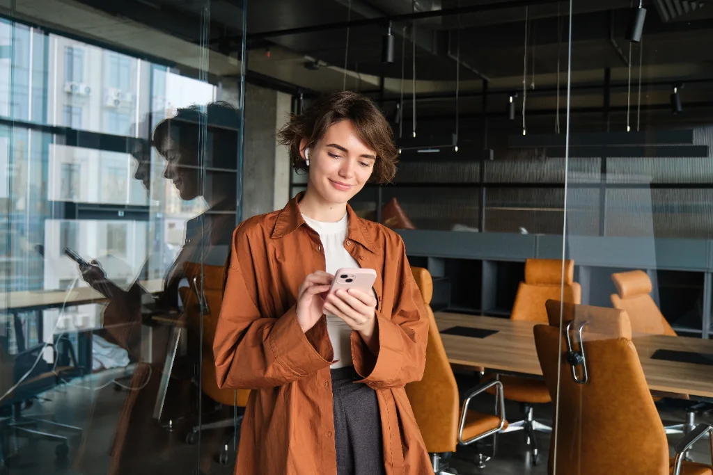 Ejecutiva enviando un mensaje SMS desde su smartphone en la oficina