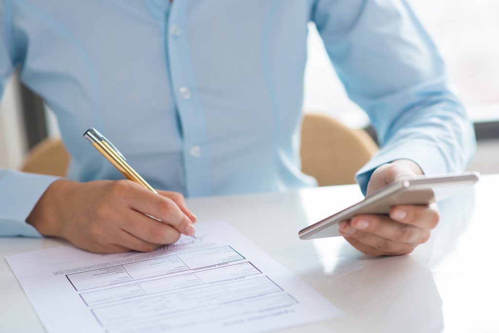 Mujer firmando un documento mientras sostiene su celular