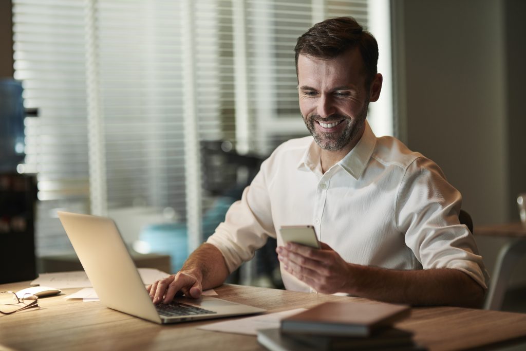 SMS vs WhatsApp vs email para notificaciones críticas: comparativa para empresas Ejecutivo trabajando con celular y laptop en su escritorio