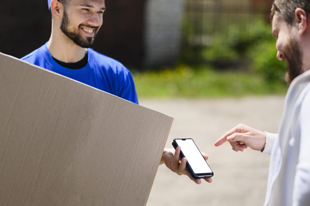 Repartidor entregando un paquete mientras el cliente confirma en su celular